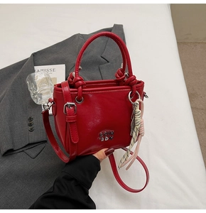 Détail d'un sac seau en cuir rouge avec lettres en métal et pendentif tissé