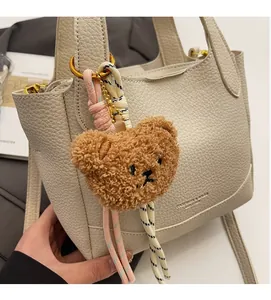 Detail of beige lychee leather handbag with a cute brown plush bear charm accessory