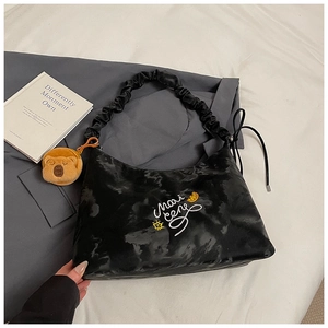 Dettaglio borsa hobo nera moiré con ricamo, tracolla arricciata e ciondolo orsetto