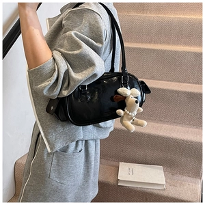 Détail d'un sac Boston noir brillant avec un pendentif chiot beige sur le côté