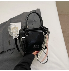 Détail du sac seau noir avec logo métallique et nœud de corde décoratif sur une veste blazer