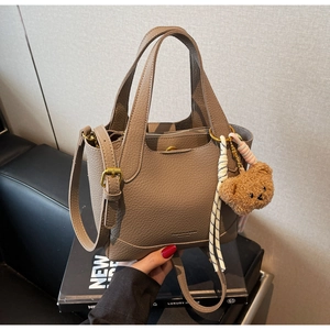 Detail of taupe bucket bag with bear pendant and fashion brand logo on front