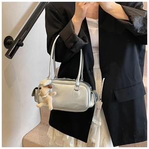 Détail du sac à main argenté métallisé avec peluche de chiot porté sur un blazer noir