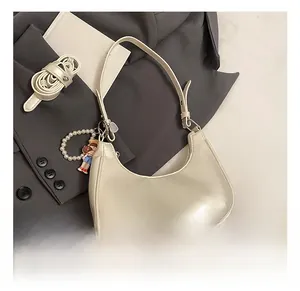 Detail of cream baguette bag featuring fashion logo, pearl chain and cute doll charm