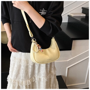 Detail of light yellow crescent bag with pearl chain and cute charm on wooden stairs