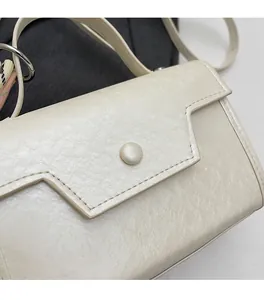 Close-up of minimalist cream square bag showing soft pleated texture and round button