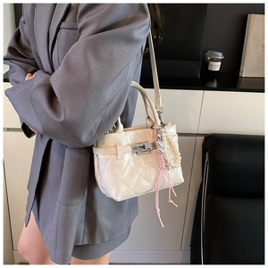 Détail d'un sac bandoulière matelassé blanc avec breloque perle et pompon rose sur blazer