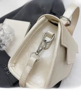 Close-up of shiny silver-tone metal clasp and cream crossbody bag leather texture