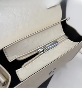 Detailed close-up of smooth silver metal zipper on ivory white textured leather handbag