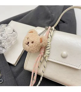 Close-up of a brown fluffy teddy bear bag charm with woven rope detail on white leather bag