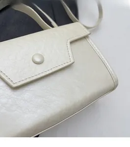 Detail of off-white faux leather handbag featuring precision stitching and smooth button