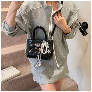 Détail du sac à main noir brillant avec fermoir métallique et charm en perles étoiles