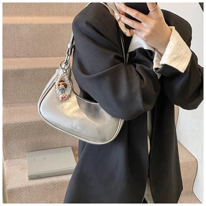 Detail of silver metallic crescent bag with pearl charm worn over a black blazer
