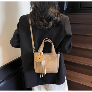Detail of light brown lychee grain leather tote bag with cute plush bear charm decoration
