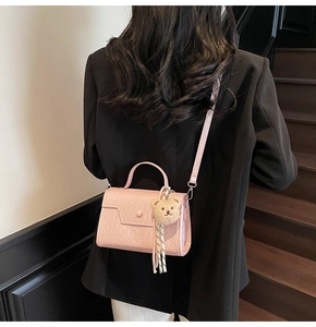 Detailed side view of pink crossbody bag with plush bear charm and black white strap