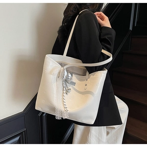 Detail of cream tote bag with embossed textures, lace trim, and decorative silver bow