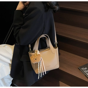 Beige litchi grain bucket bag detail with golden logo and brown plush bear charm