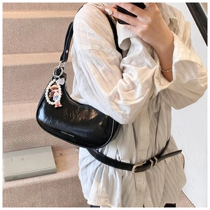 Detail of glossy black patent leather dumpling bag with pearl doll charm and fashion print