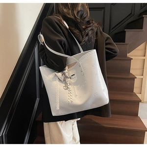 Detail view of light-colored faux leather tote bag with embossed patterns and bow pendant