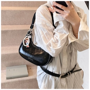 Detail of black crescent bag featuring white stitching and pearl cartoon doll charm