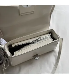 Detail view of white lychee leather bag interior with silver zipper and pearl chain accessory