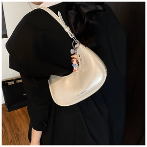 Detail of cream crescent shoulder bag with doll pendant and pearl chain on a model