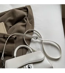 Detail view of a white crossbody bag with rotating metal lock and adjustable shoulder strap