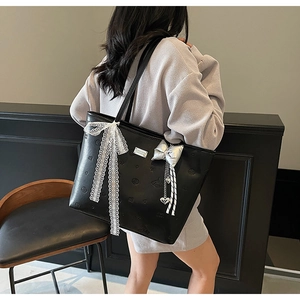 Detail of black tote bag with embossed patterns, lace bow, and silver heart charm