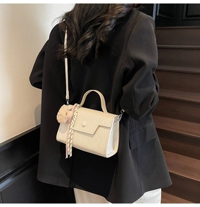 Chic beige crossbody bag with plush bear charm and silk scarf on a model's outfit