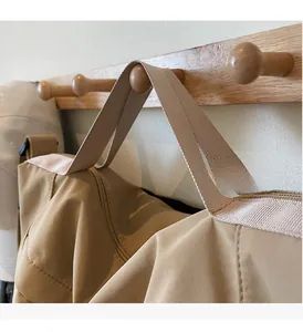 Detail of khaki tote bag with reinforced webbing handles hanging on a wooden hook