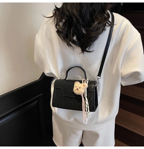 Detail of a shiny black mini square bag with a cute plush bear charm on white hoodie