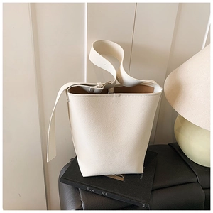 Détail d'un sac seau en cuir crème minimaliste avec texture grainée sur une chaise