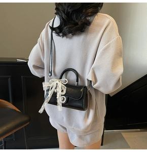 Detail showing glossy black square handbag with white lace bow and pearl chain charm