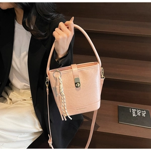 Détail d'un sac seau rose avec fermoir doré et accessoire gland tissé bohème