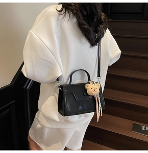 Detailed view of a black crossbody flap bag with a cute plush bear charm on a model