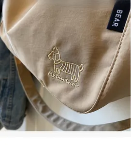 Detailed close-up of animal embroidery and BEAR woven label on beige canvas tote bag