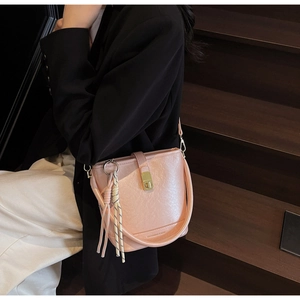 Sac seau rose avec fermoir en métal doré et détail de gland tressé sur texture cuir