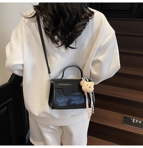Detail of black glossy handbag with pleated texture and cute cream teddy bear charm