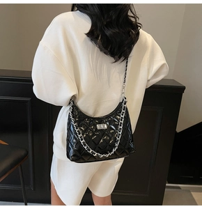 Detail of a black quilted hobo bag with silver chain and metal twist lock on a model