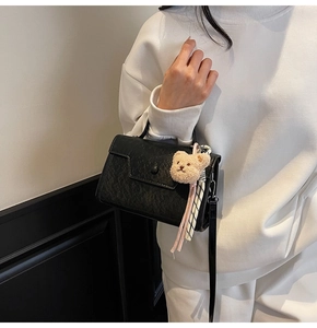Detail of black textured handbag with plush bear charm and checkered silk scarf accent
