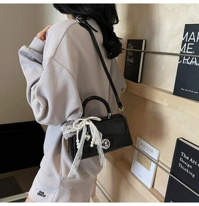 Detail of black glossy handbag with lace bow, pearl chains, and silver twist lock