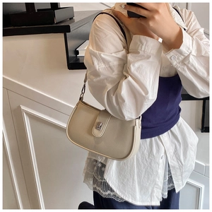 Close-up of cream leather shoulder bag with metallic buckle worn by a model in casual style