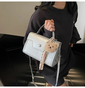 Detail of silver metallic handbag with round buckle and cute brown plush bear charm
