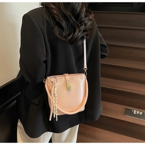 Sac seau en cuir rose avec boucles dorées porté par un mannequin sur un escalier