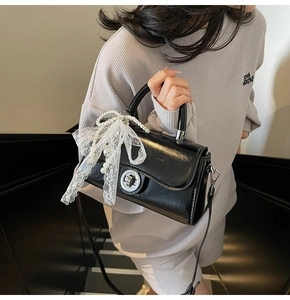 Detail view of black glossy mini handbag with pearl and lace bow charm on model