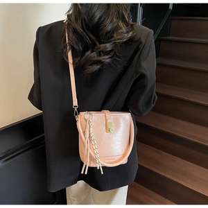 Sac seau rose avec texture cuir et fermoir doré porté par un mannequin en blazer noir