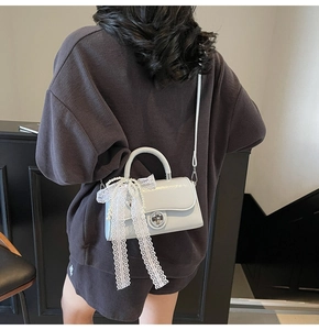 Detail of white glossy crossbody bag with lace ribbon and pearl chain on a model