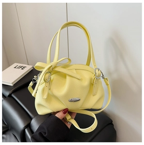 Détail du sac en cuir grainé jaune clair avec nœud décoratif et finitions argentées