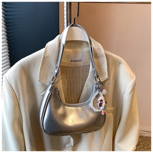Detail of silver metallic hobo bag with a decorative pearl charm on a beige blazer