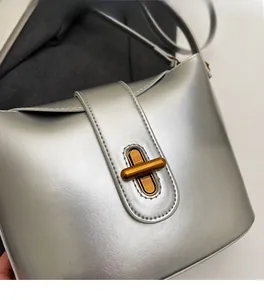 Close-up of silver crossbody bag featuring a premium glossy leather and gold twist lock